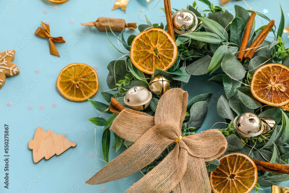 Beautiful Christmas wreath decorated with bells, orange slices and cinnamon on color background, clo