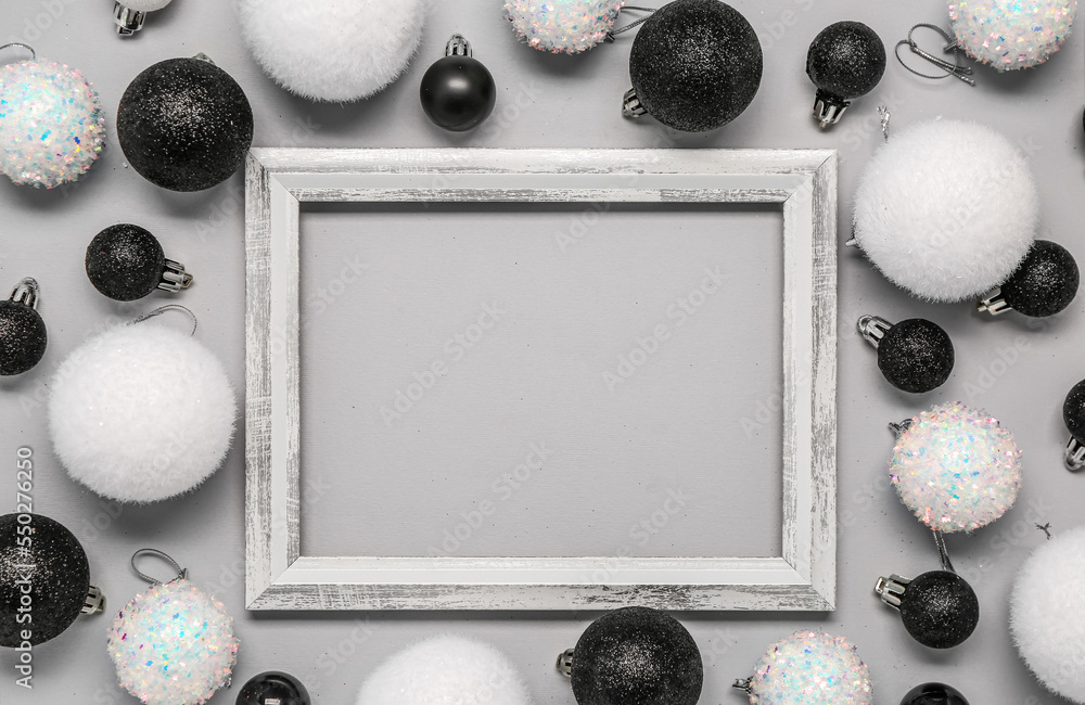 Composition with empty picture frame and Christmas balls on grey background