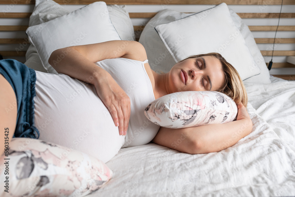 Pregnant woman restful sleeping in bed using special pillow for belly support