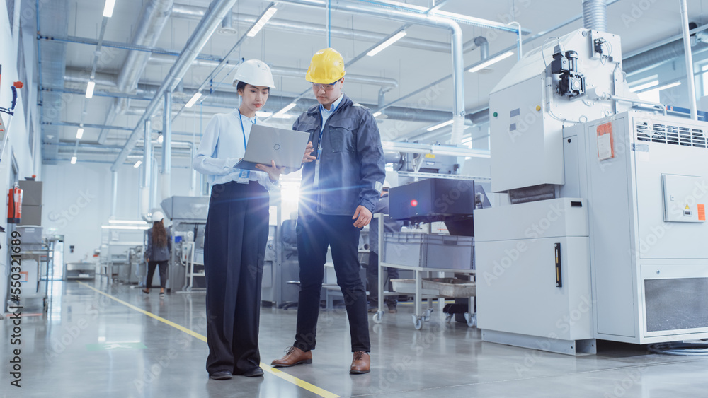 Two Young Asian Heavy Industry Engineers Walking with Their Backs to Camera, Using Laptop Computer, 