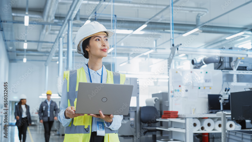 A Happy and Smiling Asian Female Engineer in White Hard Hat Standing with Laptop Computer at Electro