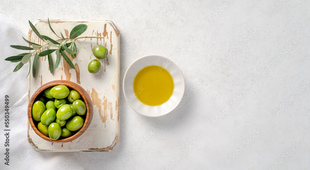 Olives, olive oil in white bowl and branch of olive on white wooden board. Mockup for package. Copy 