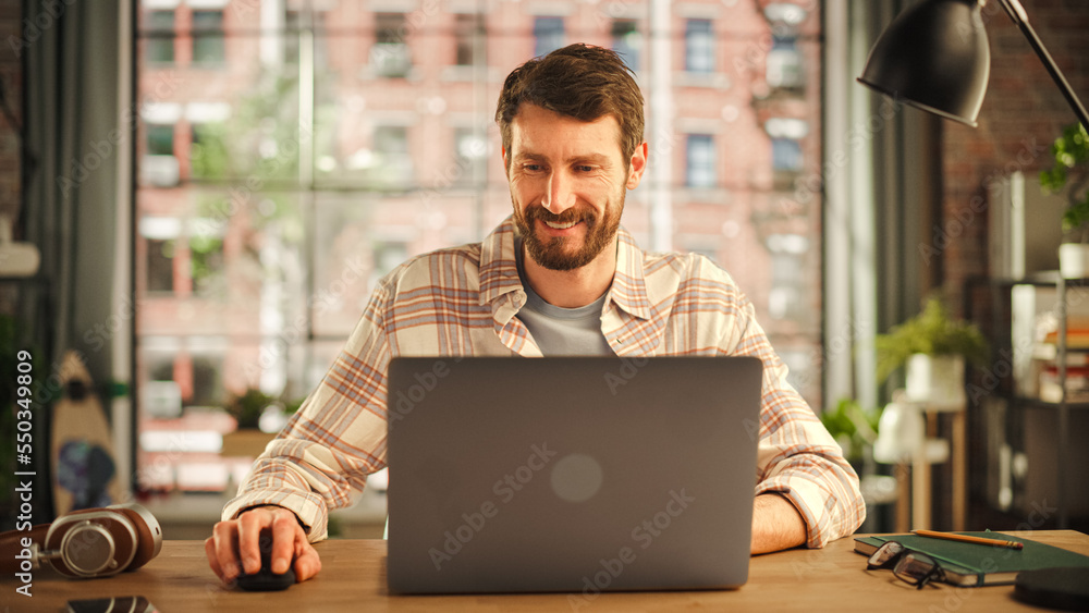 Portrait of a Handsome Man Working on Laptop Computer while Sitting in Stylish Cozy Loft Living Room