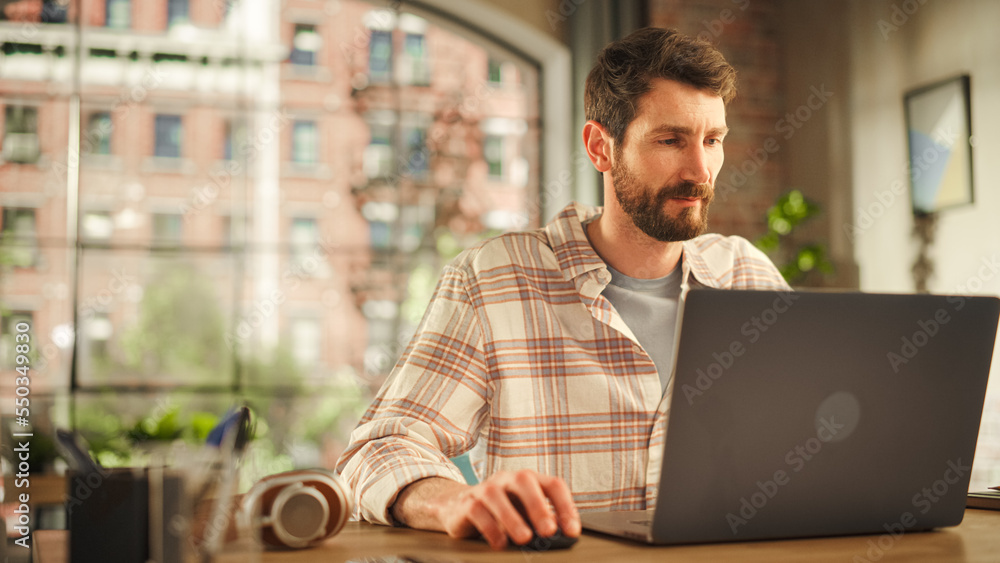 Portrait of a Handsome Man Working on Laptop Computer while Sitting in Stylish Cozy Loft Living Room