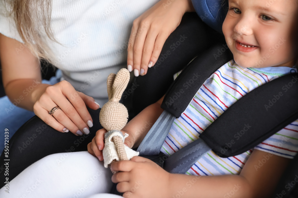 Mother and her little daughter with toy buckled in car safety seat, closeup