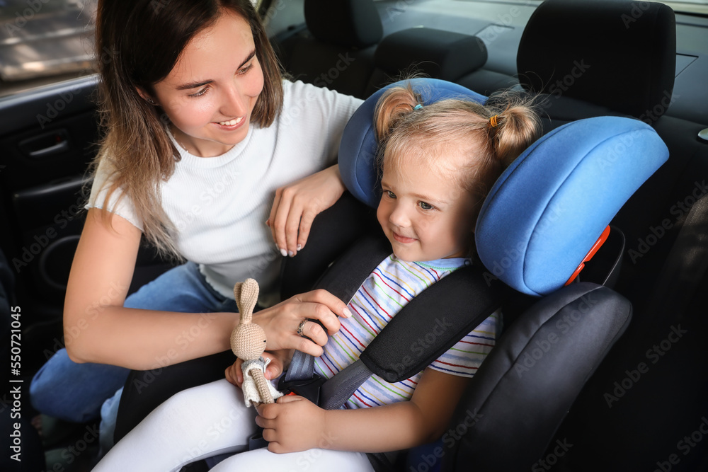 Mother and her little daughter with toy buckled in car safety seat