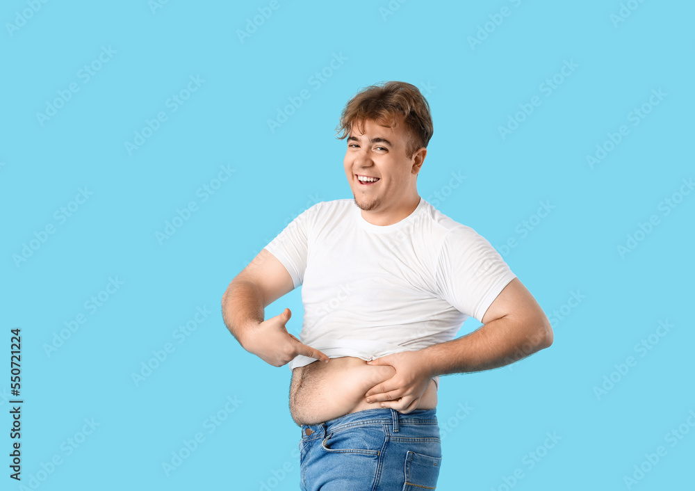 Young overweight man pointing at his belly on blue background