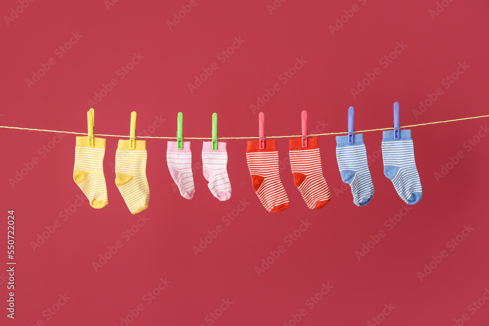 Baby socks hanging on laundry line against color background