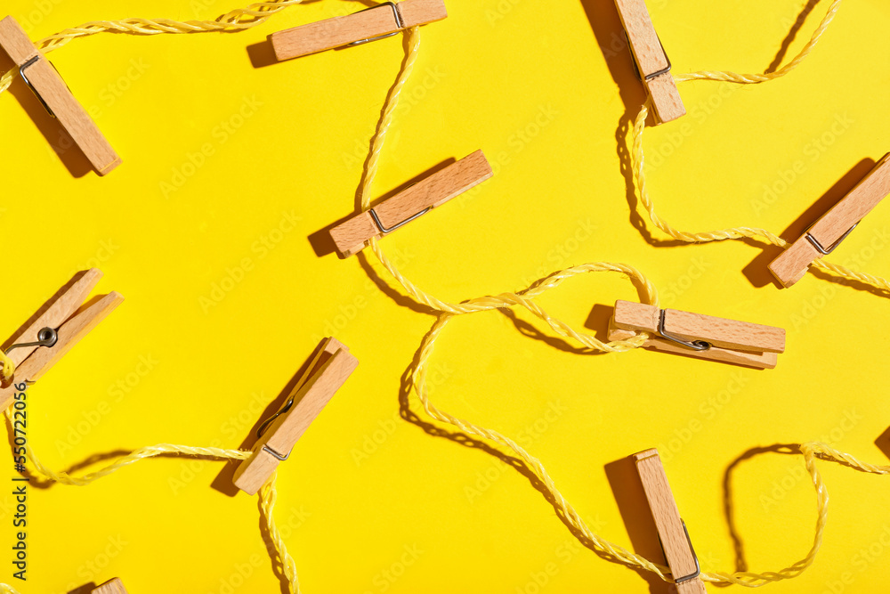 Wooden clothespins and rope on yellow background