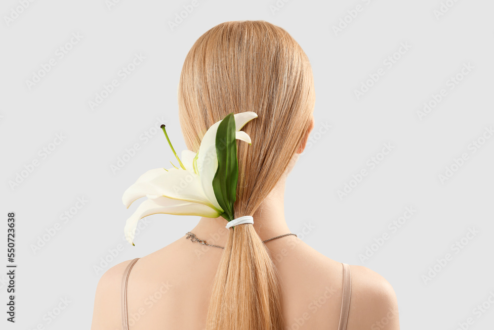 Blonde woman with ponytail and lily flower on light background