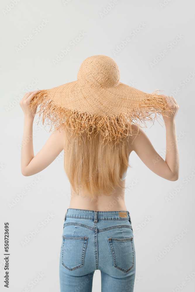 Blonde woman with long hair touching straw hat on light background