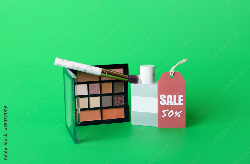 Eyeshadows with brush, perfume and sale tag on green background