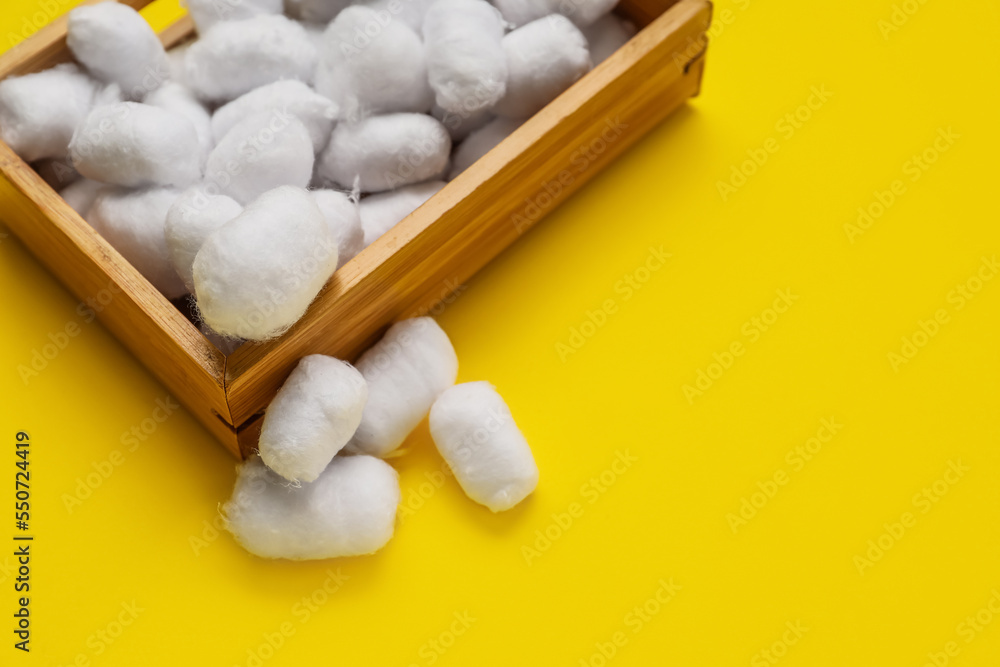 Wooden box of soft cotton balls on yellow background, closeup