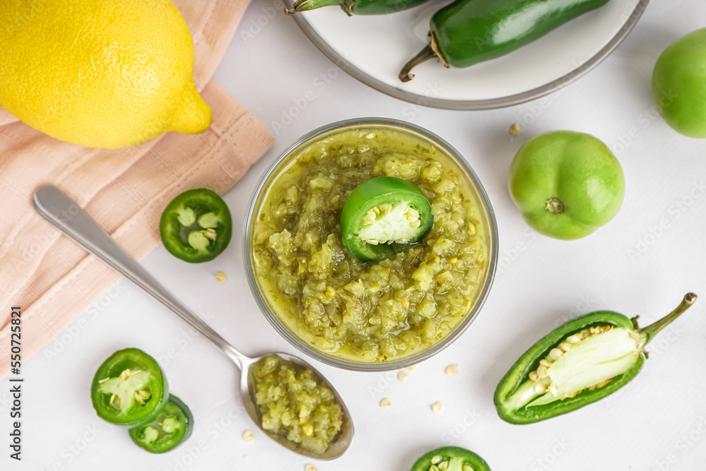 Bowl of tasty green salsa sauce and jalapeno peppers on light background