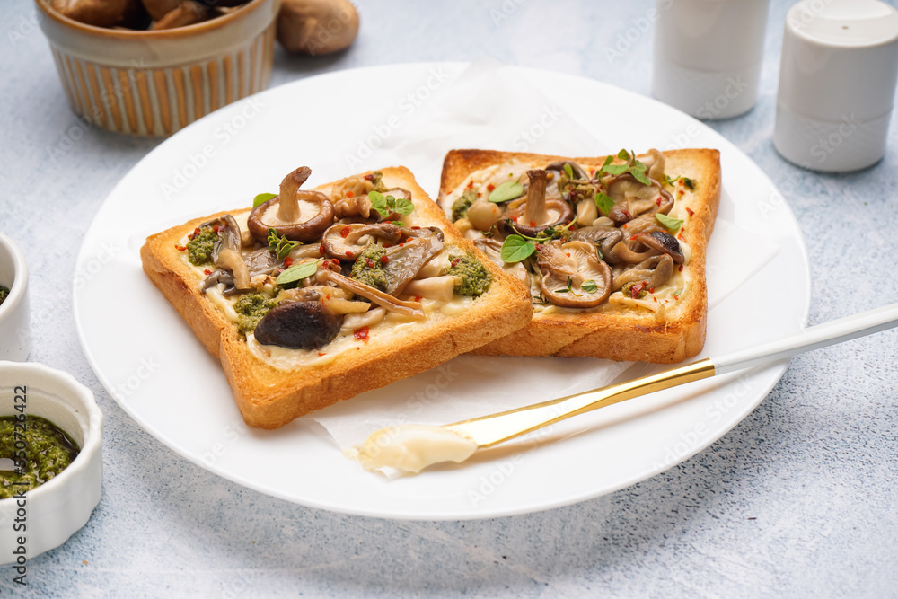 Plate of tasty toasts with cream cheese, mushrooms and pesto sauce on light table, closeup