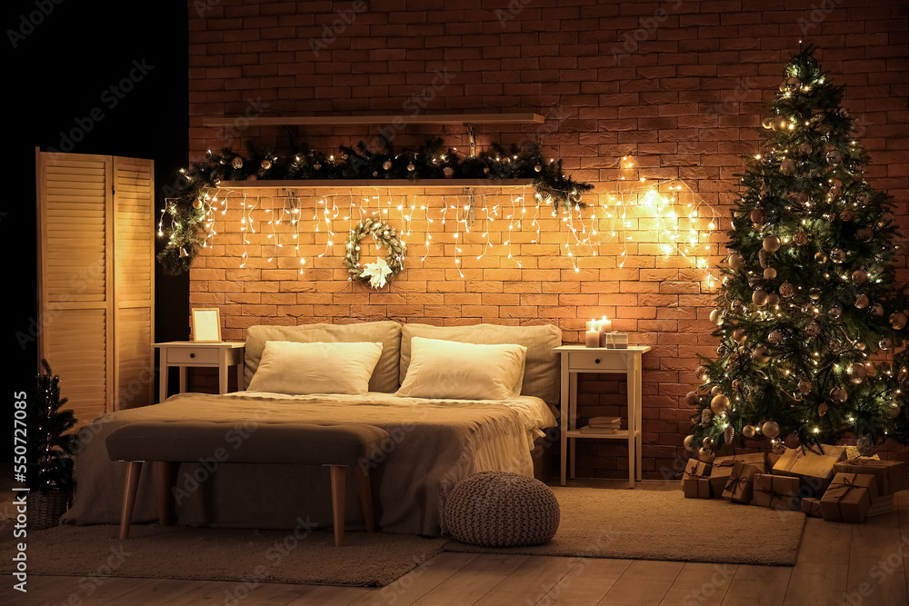 Interior of dark bedroom with Christmas trees, fir branches and glowing lights