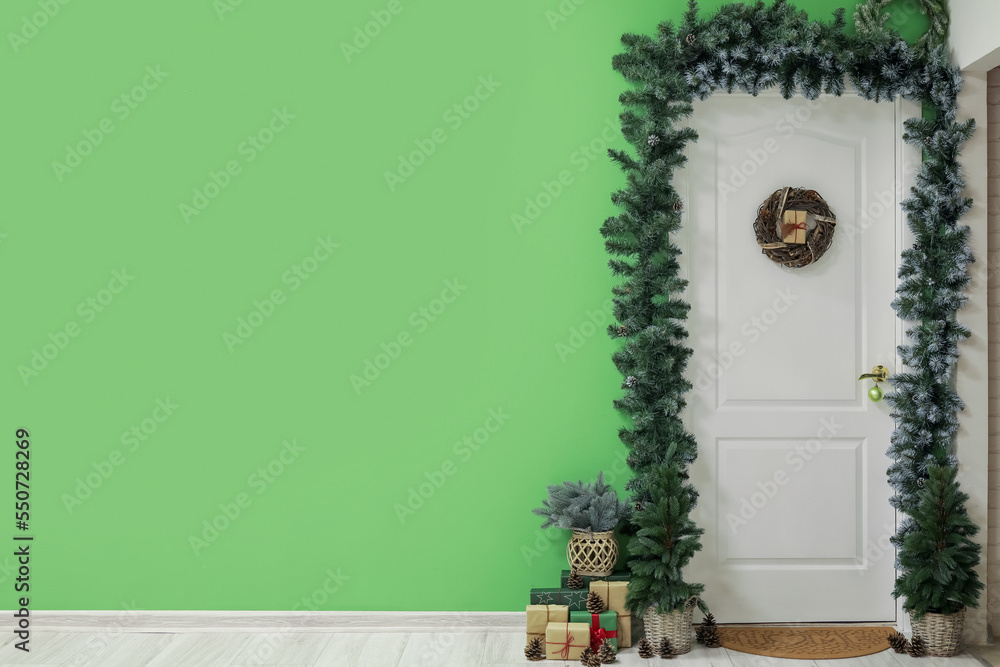 White door with Christmas wreath, fir trees, branches and presents in hall