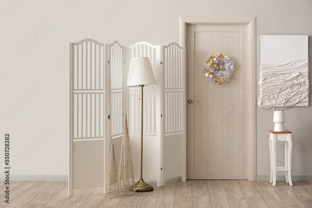 Interior of light room with wooden door, Christmas wreath and folding screen