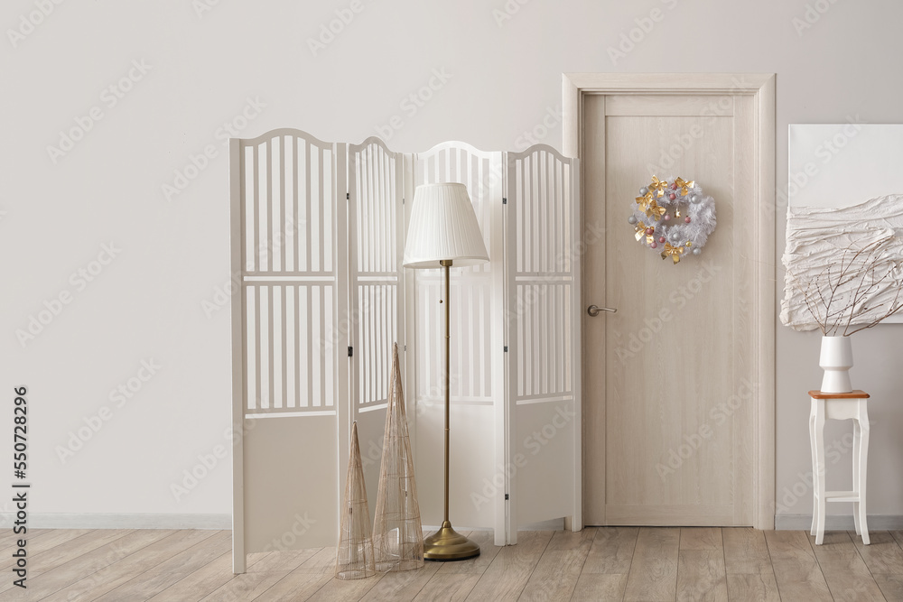 Interior of light room with wooden door, Christmas wreath and folding screen