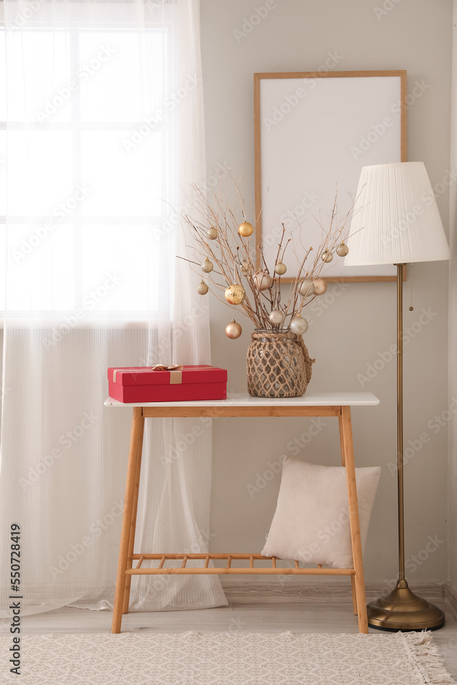 Vase with tree branches, Christmas balls and gift on table in living room