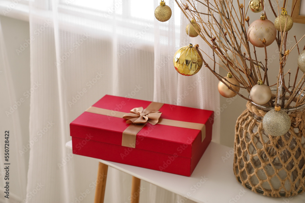 Vase with tree branches, Christmas balls and gift on table in living room, closeup