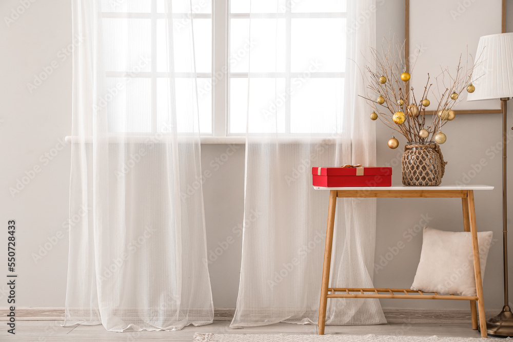 Vase with tree branches, Christmas balls and gift on table in living room