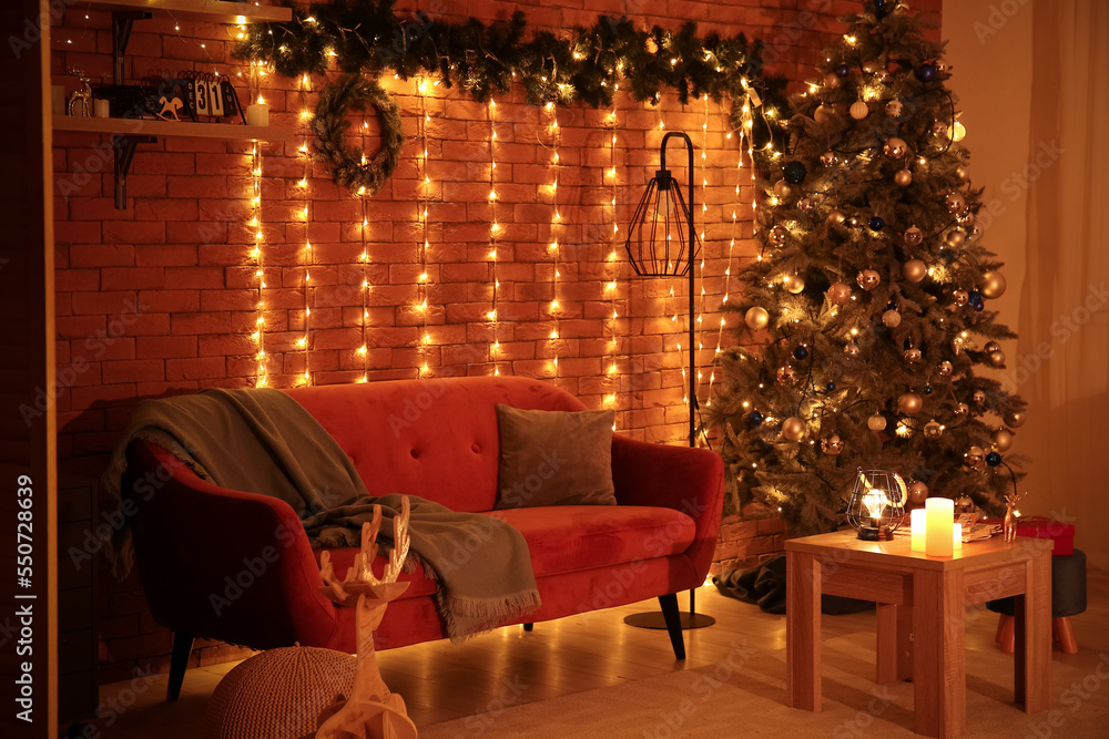 Interior of living room with Christmas tree, sofa and glowing lights at night