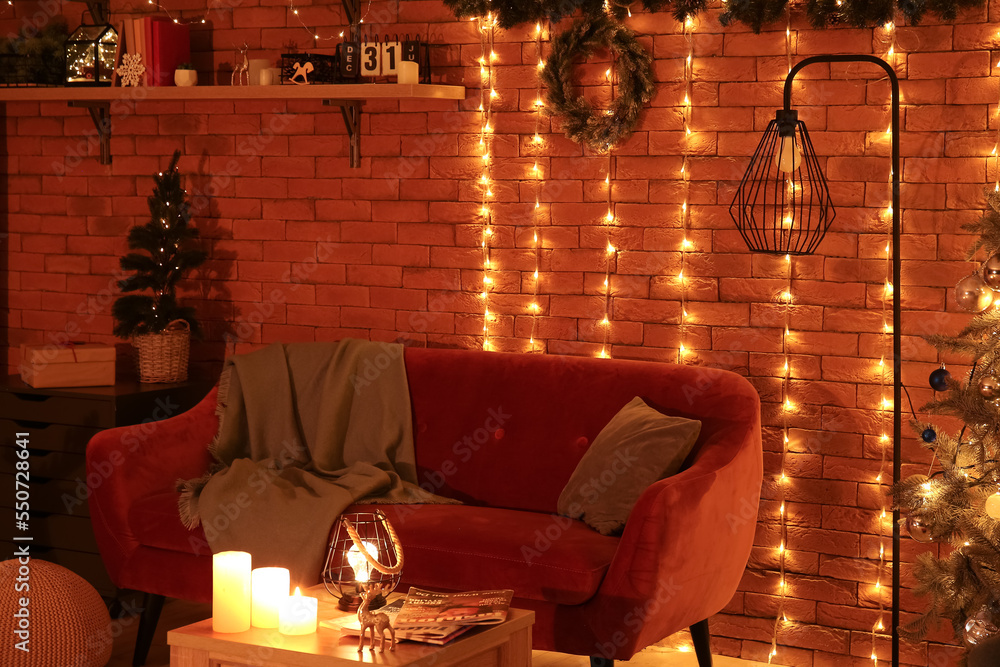 Interior of living room with Christmas wreath, sofa and glowing lights at night