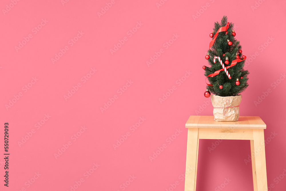 Small Christmas tree on stool near red wall