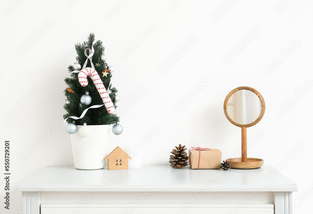 Small Christmas tree with toys, mirror and gift on shelf near light wall