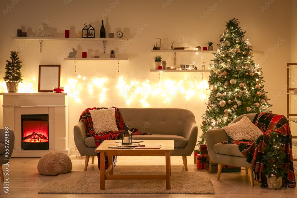 Interior of living room with glowing Christmas trees, sofa and fireplace at night