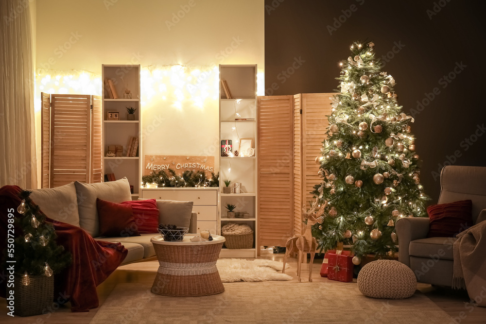 Interior of living room with glowing Christmas trees, sofa and armchair at night