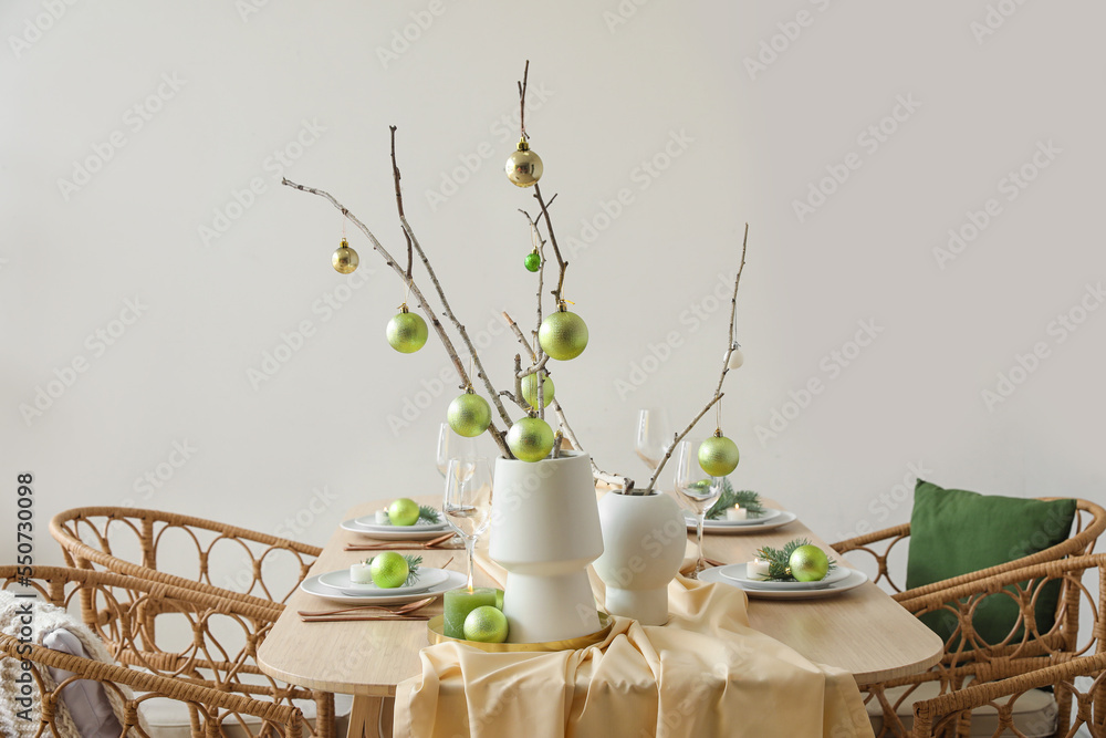 Vases with tree branches and green Christmas balls on dining table near grey wall