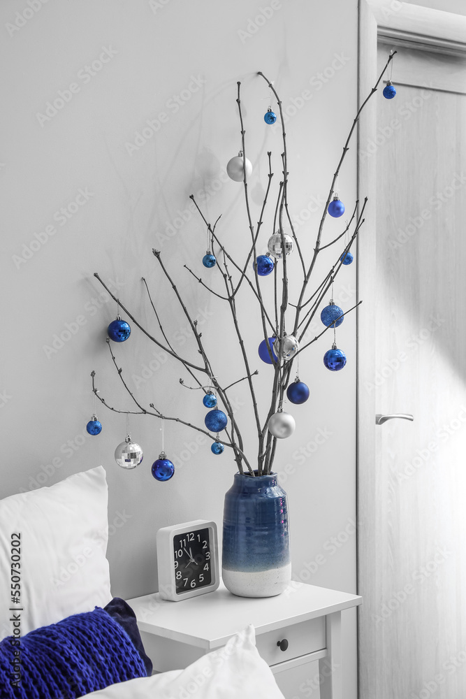 Vase with tree branches, Christmas balls and clock on table in bedroom