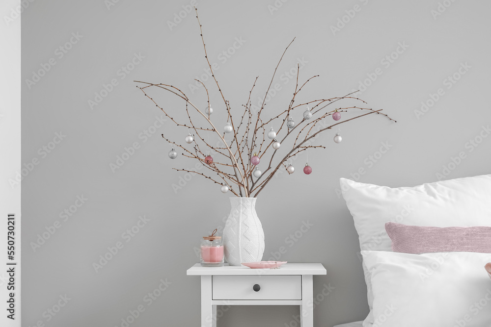 Vase with tree branches, Christmas balls, candle and jewelry on table in bedroom