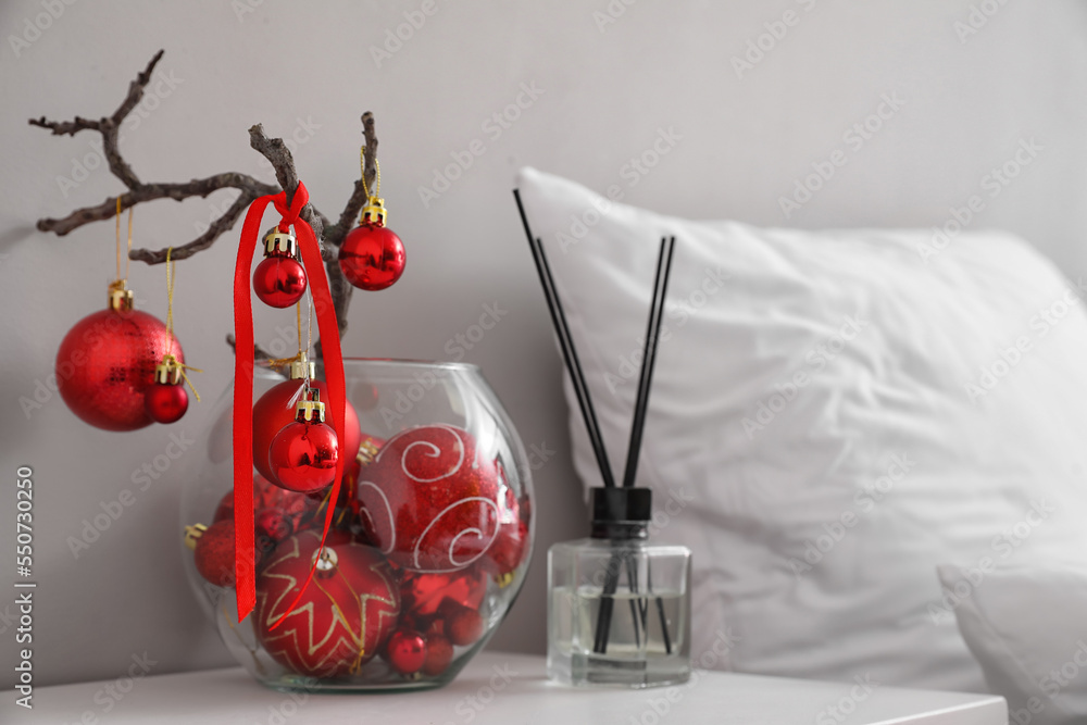 Vase with tree branches, Christmas balls and reed diffuser on table in bedroom