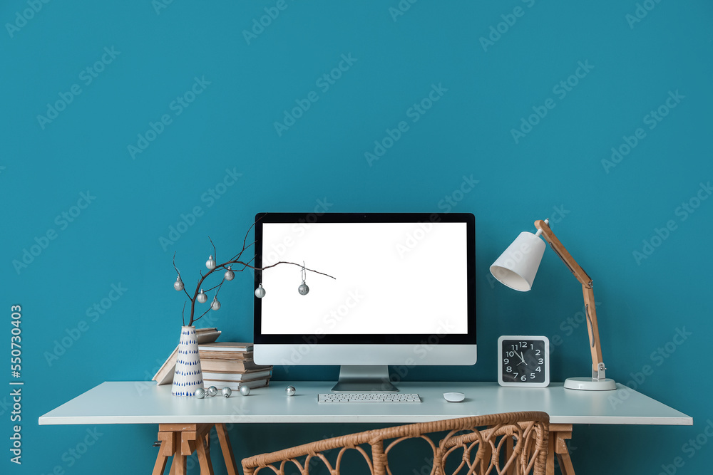 Workplace with computer, tree branches and Christmas balls in vase near blue wall