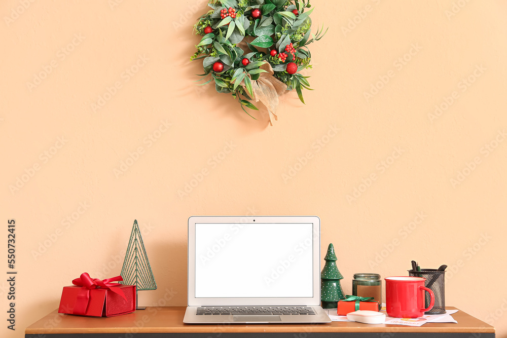 Laptop with Christmas presents and coffee cup on table near beige wall