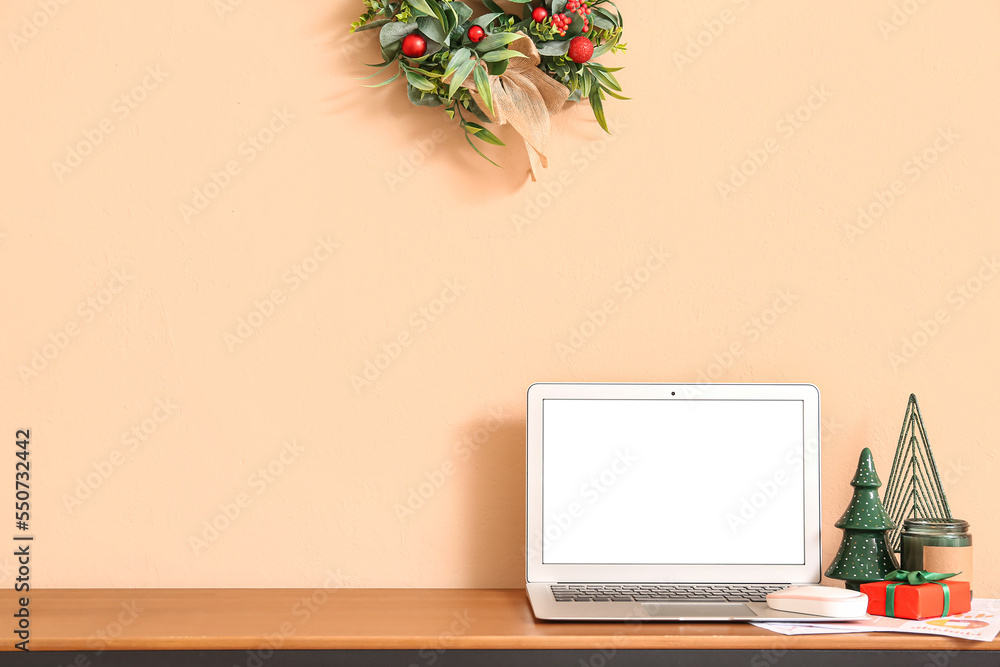 Laptop with Christmas gift and decor on table near beige wall