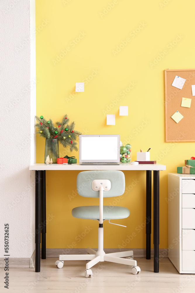 Interior of office with workplace, fir branches in vase and Christmas presents