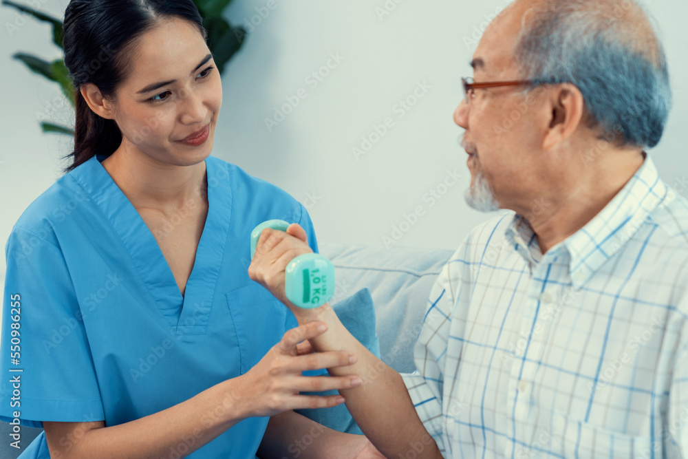 Contented senior patient doing physical therapy with the help of his caregiver. Senior physical ther