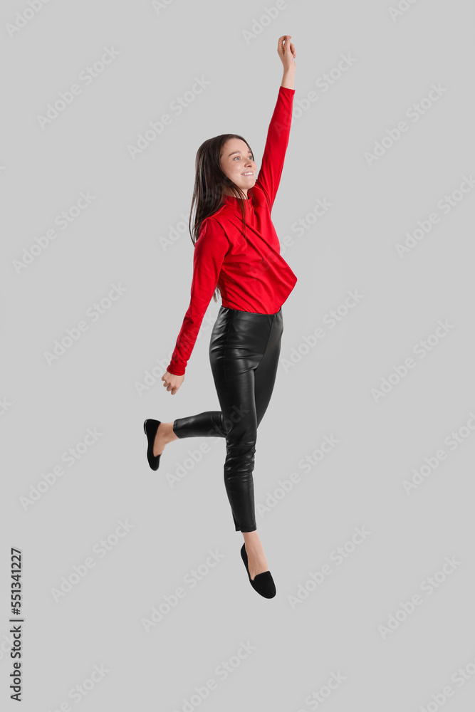 Young brunette woman in leather pants jumping on grey background