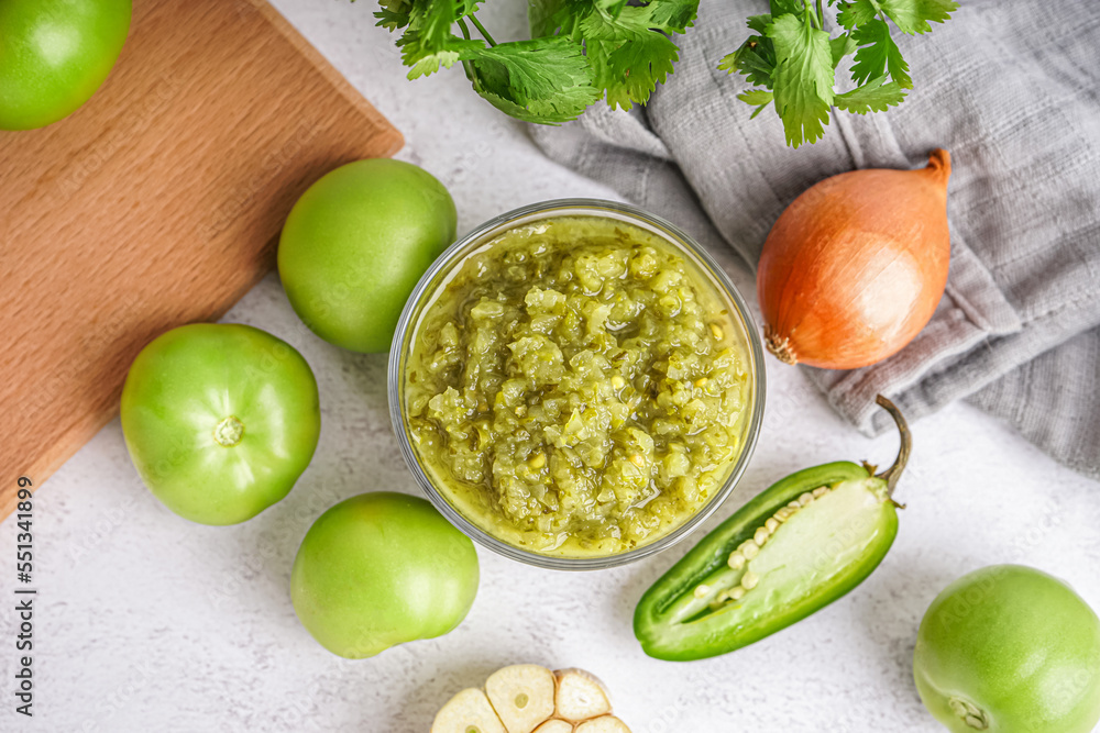 Bowl of tasty green salsa sauce with ingredients on light background