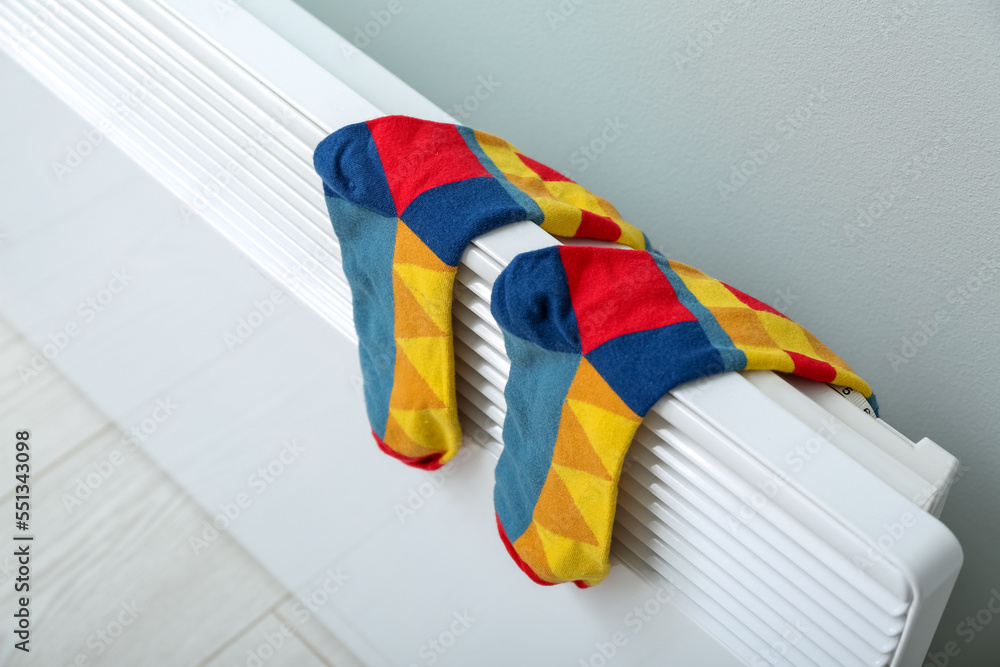 Warm socks drying on electric radiator near light wall, closeup