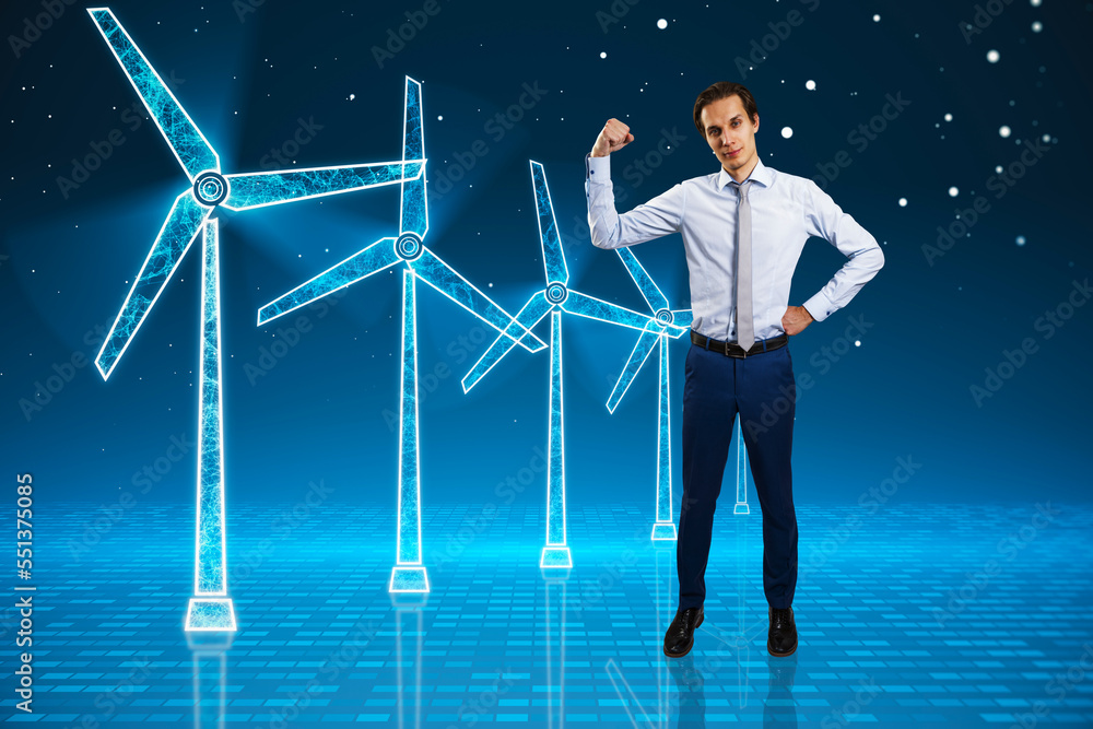 Young businessman flexing muscle and looking at glowing digital wind mill turbine hologram on blue b