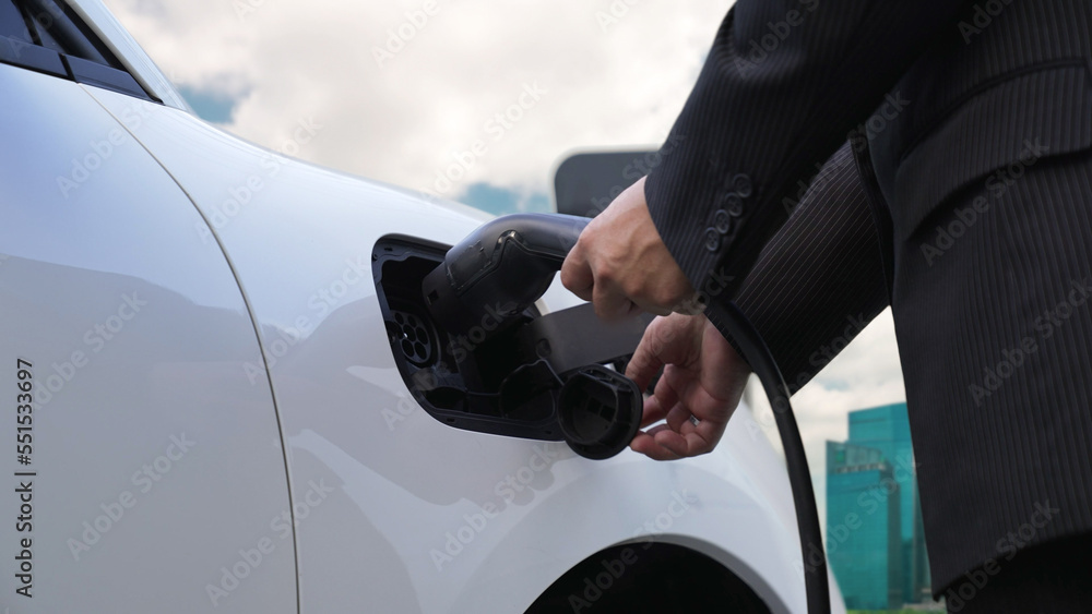 Progressive businessman recharge his electric vehicle with charger cable plug from charging station 