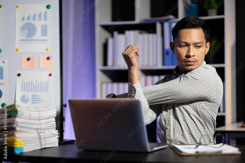 Man suffering from overwork is stretching and relaxing while working overtime in night office.