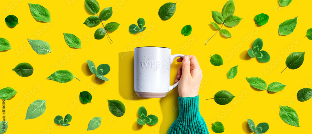 Person holding a mug with green leaves - flat lay