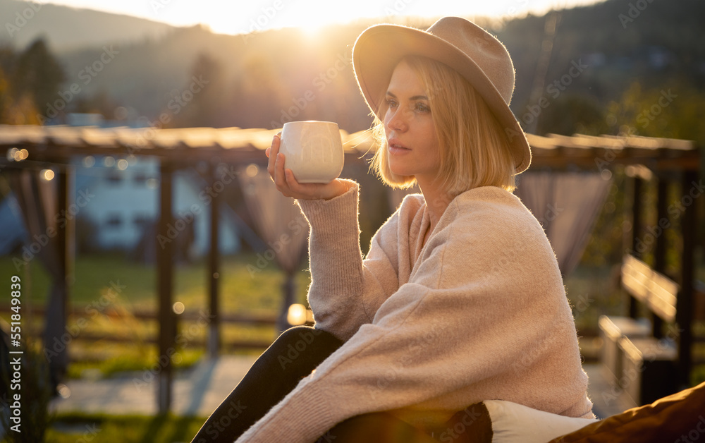 Beautiful woman in cowboy hat drinking coffee on patio in front of her house