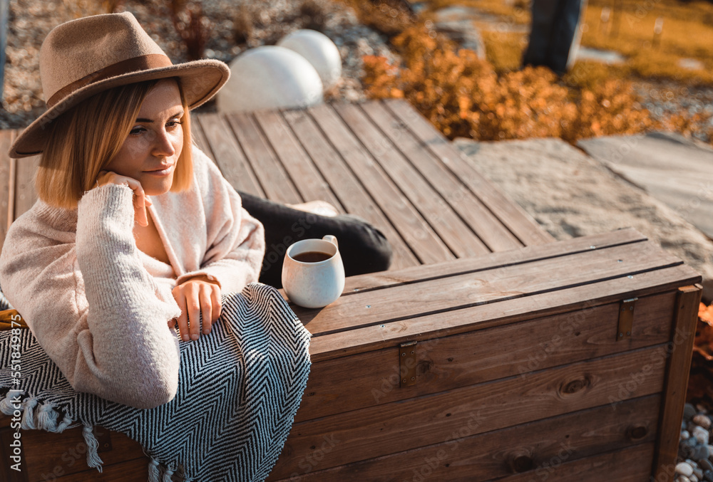 Beautiful woman in cowboy hat drinking coffee on patio in front of her house